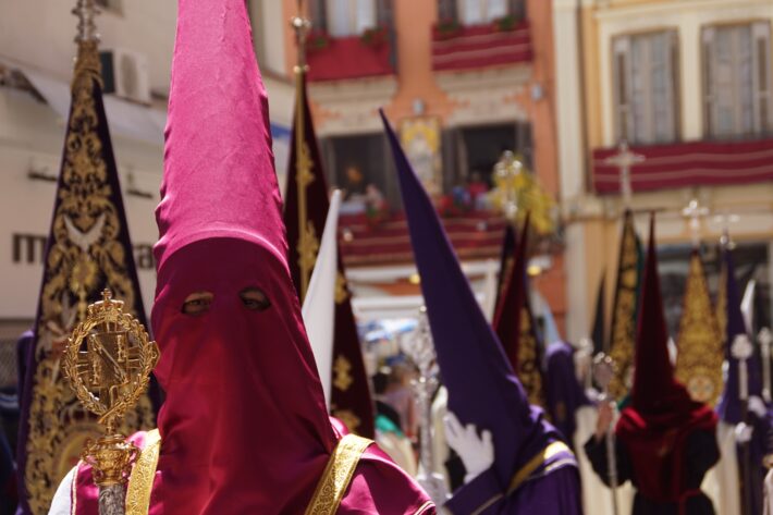 Parade of people wearing pink, purple and red tall masks during Holy Week at Malaga