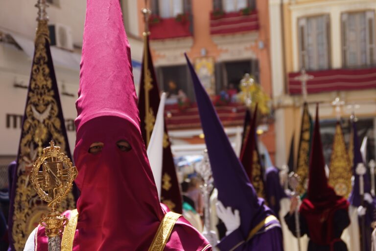 Parade of people wearing pink, purple and red tall masks during Holy Week at Malaga
